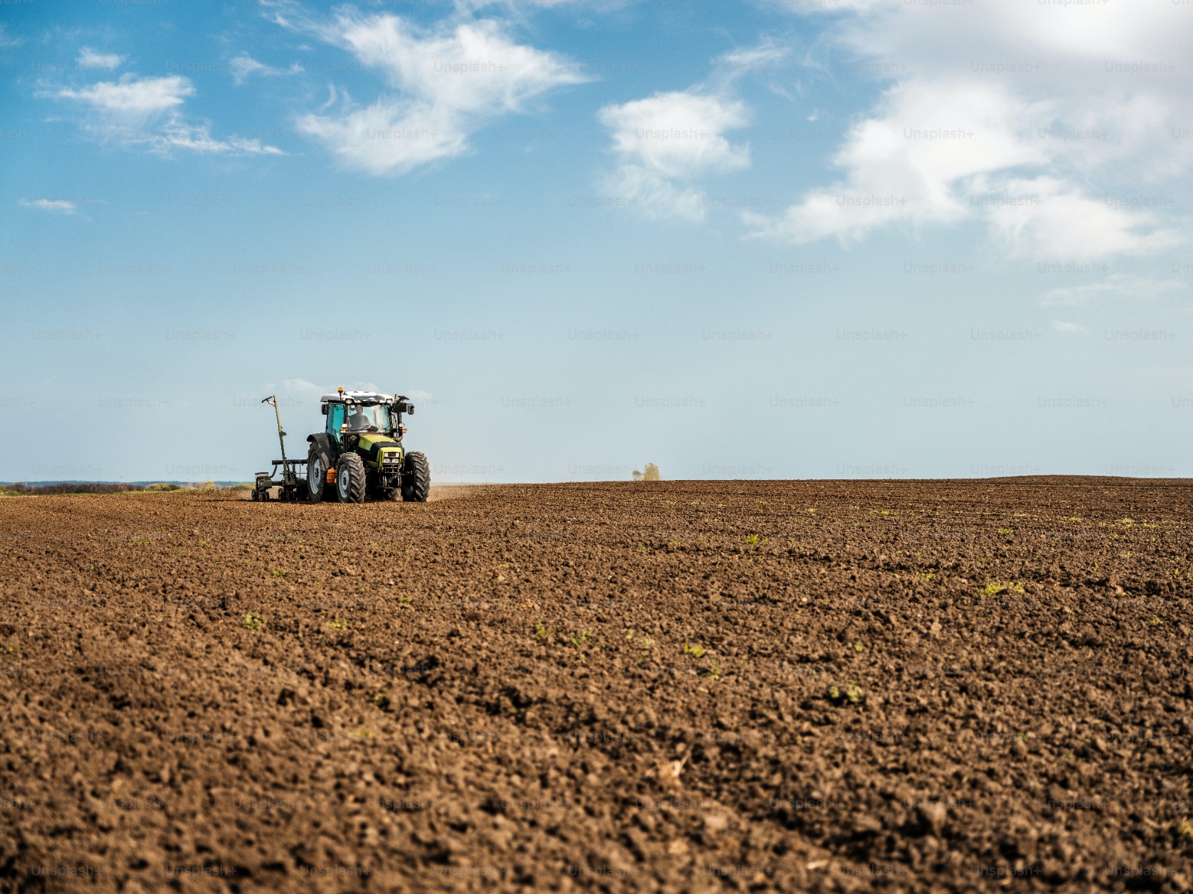 Un tracteur laboure un champ avec un ciel bleu en arrière-plan.